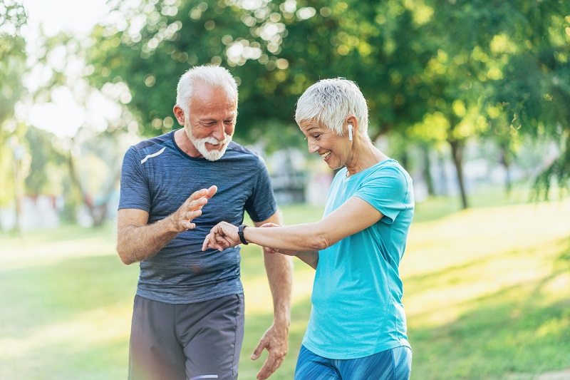Older man and woman in a park setting their activity trackers while walking to burn more calories