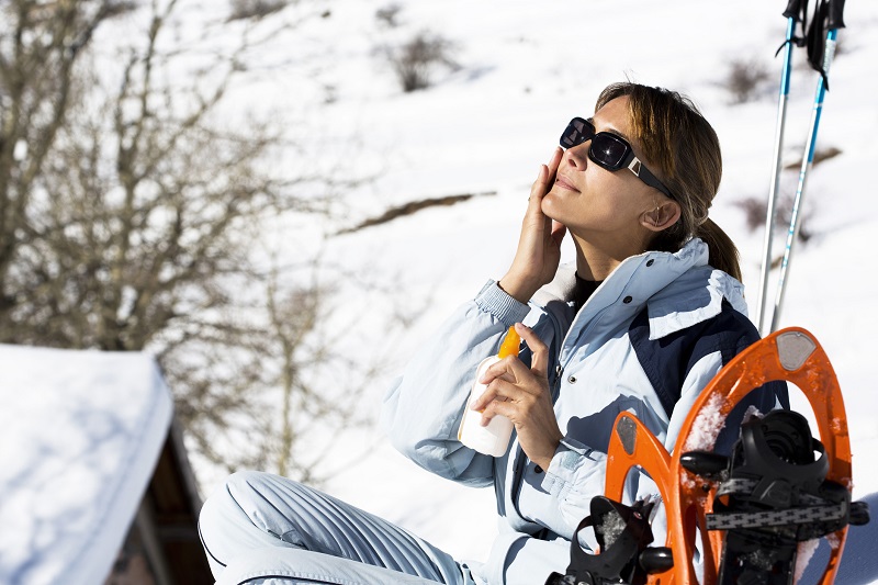 a woman applying sunscreen during a sunny day before doing winter workouts