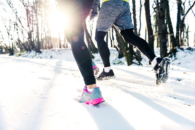 a woman and man running in the snow on a sunny day