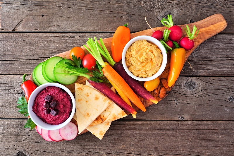 a variety of vegetables and dips on a charcuterie board