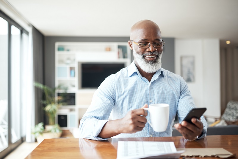 a happy older man drinking coffee while looking at his phone